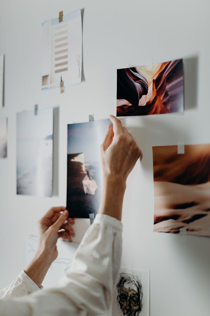 Hands arranging a mood board with various photos on an indoor wall.