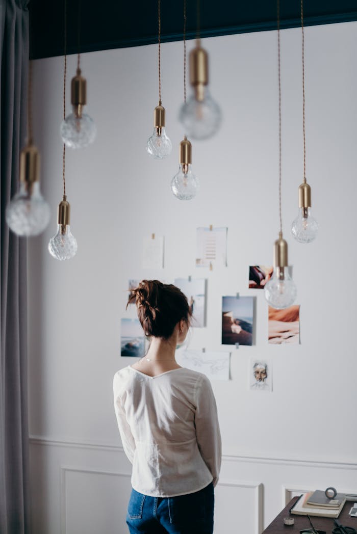 A woman stands inside, viewing an inspiring mood board, under hanging lights.